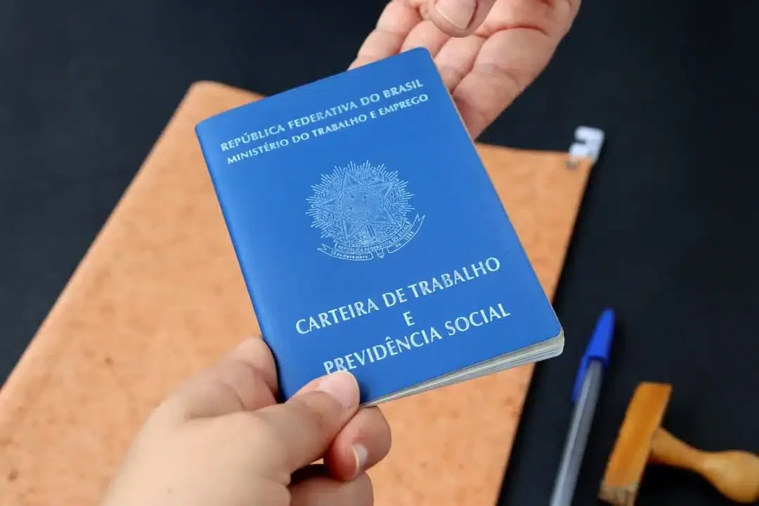 Carteira de Trabalho sendo entregue de uma pessoa para outra.