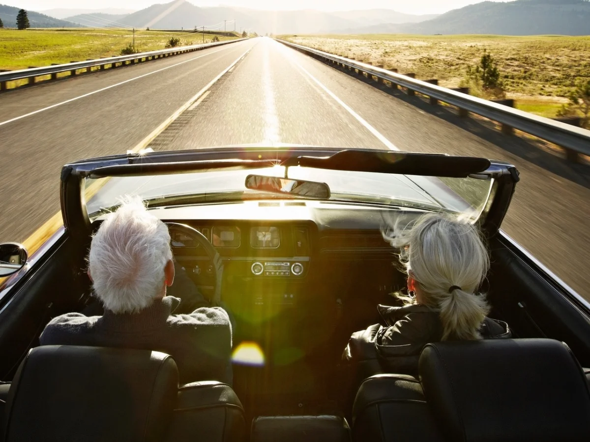 Casal de idosos dirigindo em uma estrada deserta.