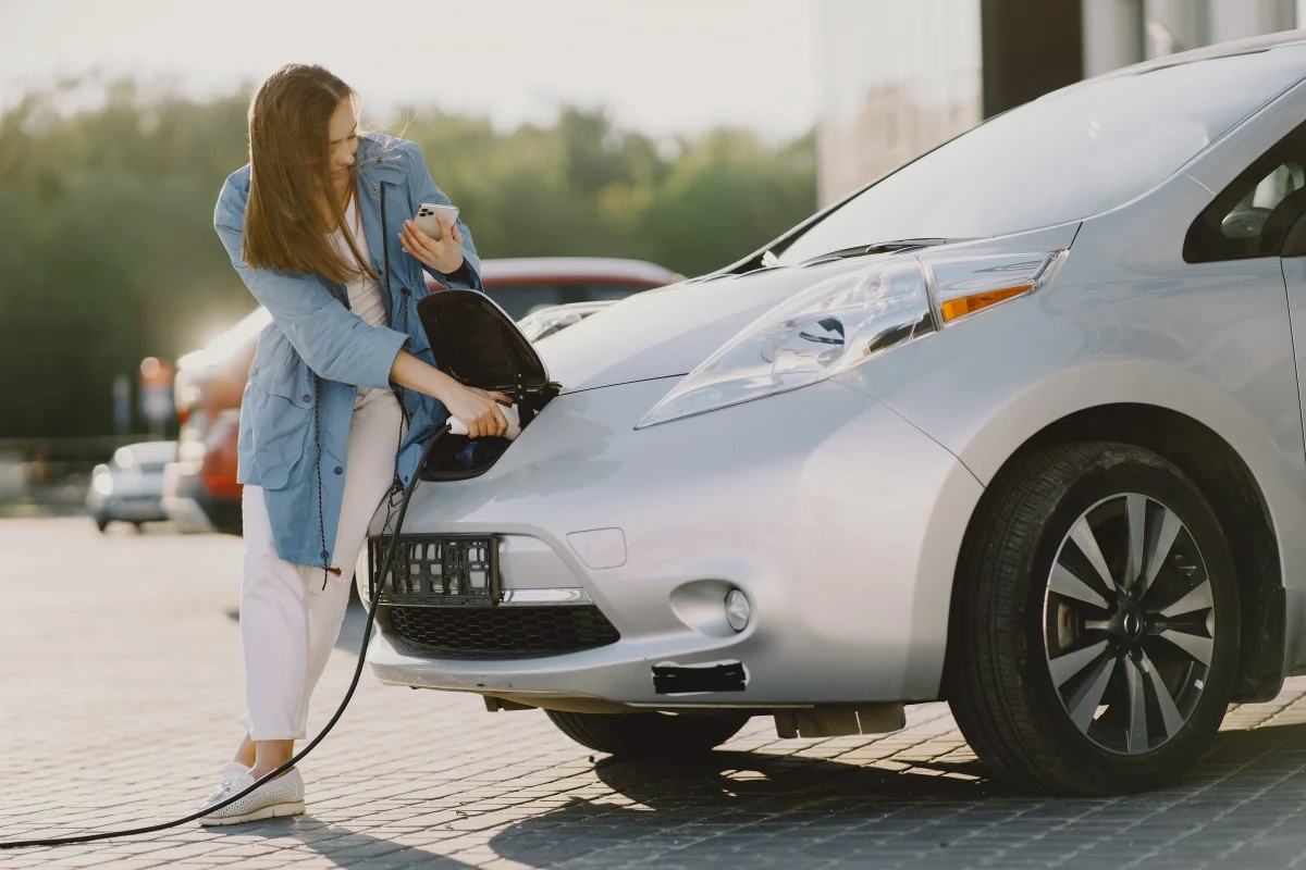 Mulher carregando um carro elétrico em posto de gasolina