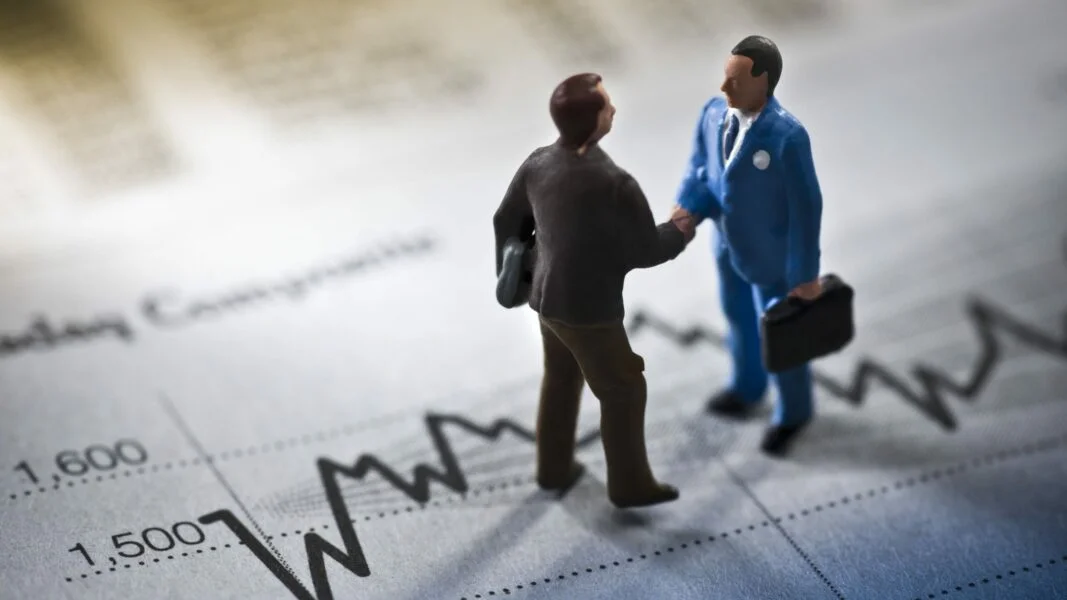Duas pessoas em um aperto de mãos sobre um gráfico financeiro.