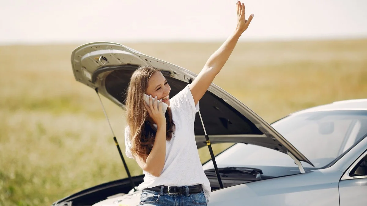 Mulher pedindo ajuda próximo a um carro quebrado.