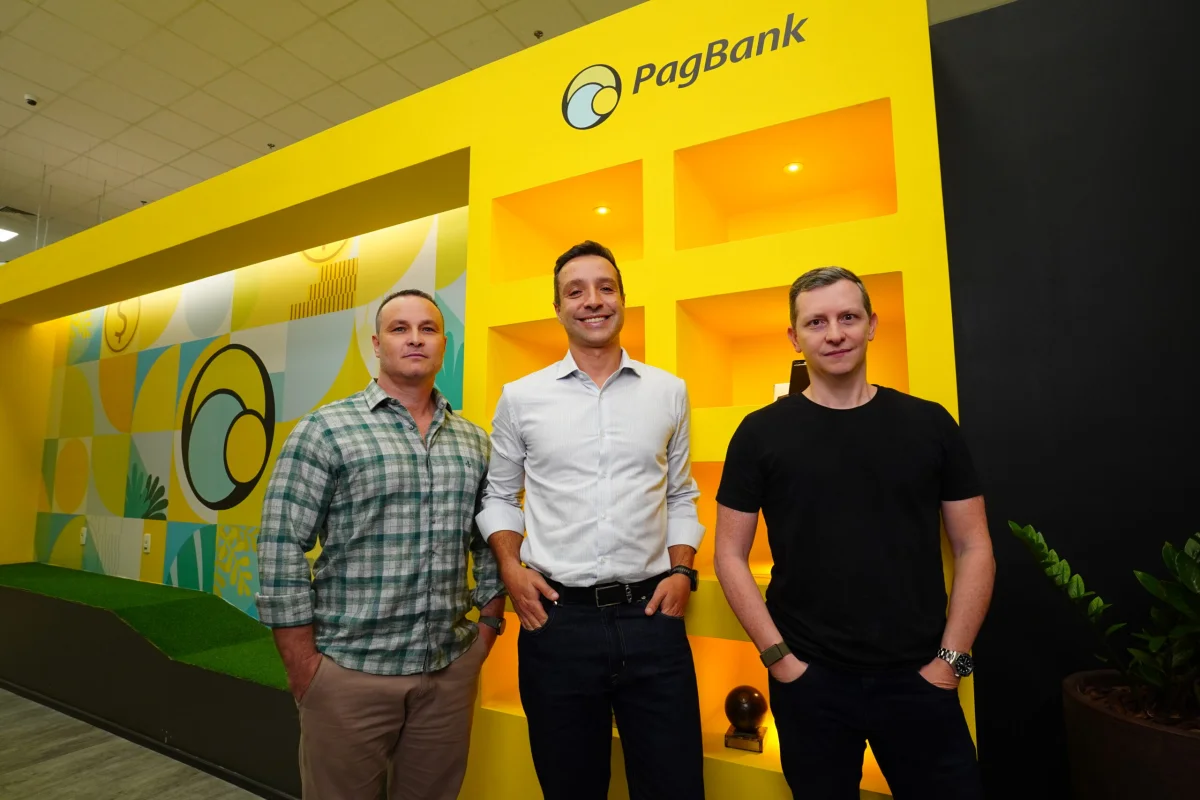 Três homens posando em frente ao PagBank.