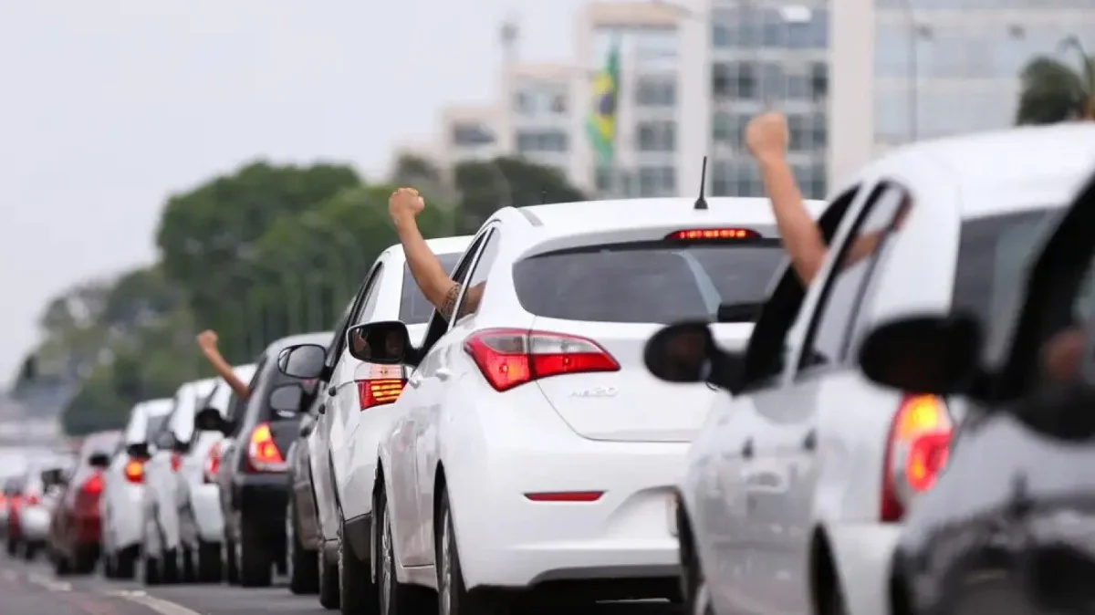 Carros enfileirados com motoristas levantando os braços